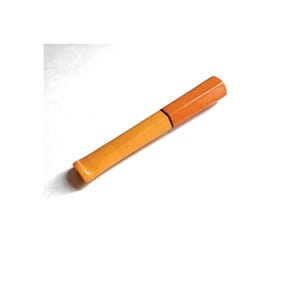May include: A two-toned orange highlighter pen. The pen has a rectangular shape with a lighter orange body and a darker orange cap. The pen is lying on a white surface.
