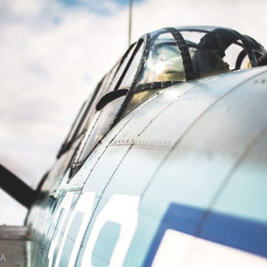 May include: Close-up of a vintage military aircraft, painted in a light blue and gray color scheme. The aircraft has a large, clear canopy and a machine gun mounted on the top. The aircraft is numbered "100" on the side.