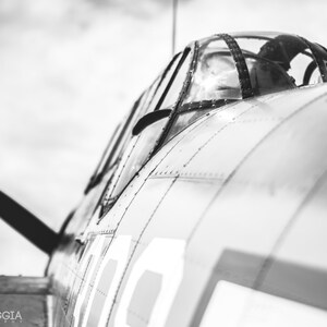 May include: A black and white photo of a vintage airplane cockpit. The cockpit is open and the pilot's seat is visible. The airplane is painted in a silver color with a black propeller.
