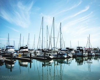 May include: A marina with a variety of sailboats and motorboats docked at the pier. The boats are all different sizes and colors, and some have flags flying from their masts. The water is calm and blue, and the sky is clear and bright.