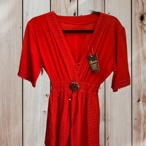 Pode incluir: Um vestido de praia vermelho de croch&ecirc; com decote em V, mangas curtas e fecho de bot&atilde;o. O vestido tem uma borda de renda e uma cintura com cord&atilde;o. A etiqueta diz "Oasis".