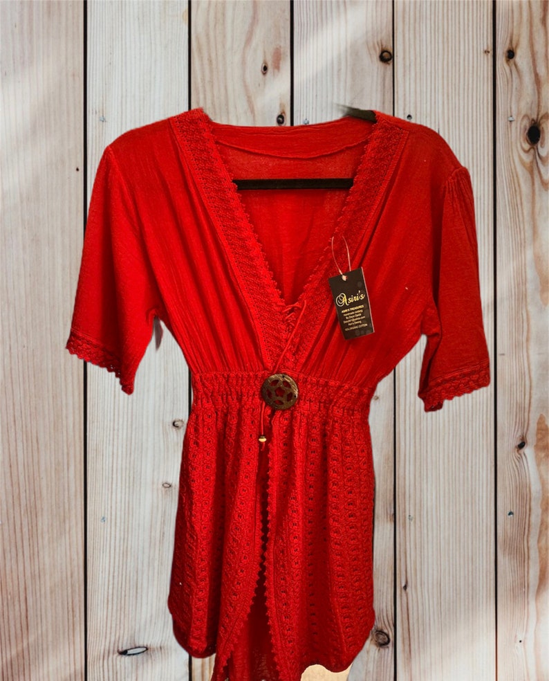 Pode incluir: Um vestido de praia vermelho de croch&ecirc; com decote em V, mangas curtas e fecho de bot&atilde;o. O vestido tem uma borda de renda e uma cintura com cord&atilde;o. A etiqueta diz "Oasis".