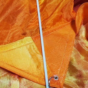 May include: A white fabric streamer with a red, orange, and yellow gradient. The streamer is attached to a white pole with a silver clip.
