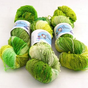 Może przedstawiać: Kolekcja zielonych i żółtych motków przędzy. Przędza ma różne odcienie zieleni, od jasnego do ciemnego, z kilkoma żółtymi akcentami. Każdy motek ma etykietę z tekstem i obrazkiem z kreskówki.