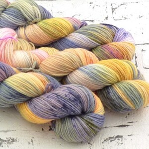 Könnte beinhalten: Eine Garnrolle in den Farben Lila, Gelb und Grün. Das Garn ist handgefärbt und hat ein buntes Farbmuster.