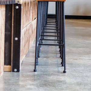 May include: A row of black metal bar stools with wooden seats line up against a wooden counter with a concrete top.