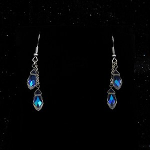 K&ouml;nnte beinhalten: Ein Paar silberne Ohrringe mit drei blauen, schillernden Kristalltropfen.