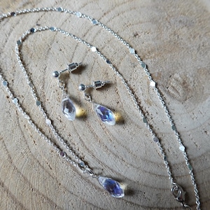 May include: A silver chain necklace and matching earrings with iridescent teardrop-shaped crystals.