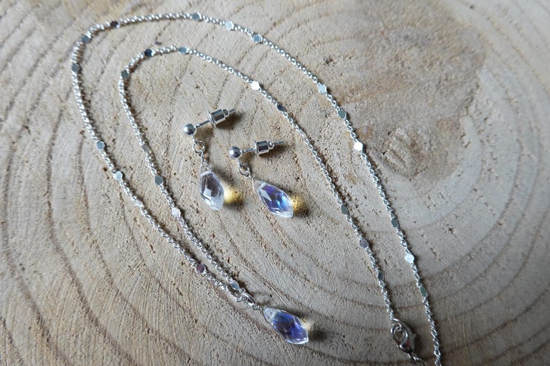 May include: A silver chain necklace and matching earrings with iridescent teardrop-shaped crystals.