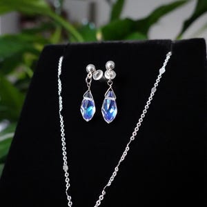 May include: A silver necklace and earrings set with teardrop-shaped blue crystals. The necklace is a delicate chain with a small pendant.