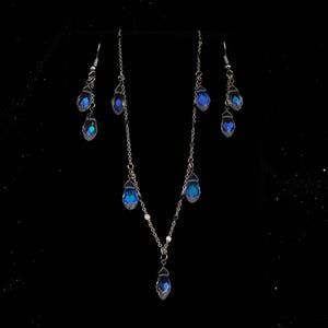 K&ouml;nnte beinhalten: Ein silbernes Halsketten- und Ohrring-Set mit blauen, tropfenf&ouml;rmigen Kristallen. Die Halskette hat einen einzelnen Kristall-Anh&auml;nger und die Ohrringe haben jeweils zwei Kristalle.