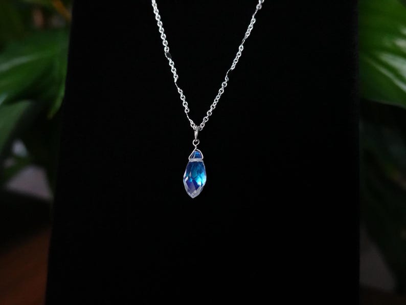 May include: A silver chain necklace with a blue iridescent crystal pendant.