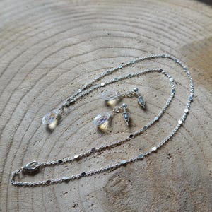 May include: A silver necklace and earrings set with clear crystal teardrop pendants. The necklace is a delicate chain with small silver beads.