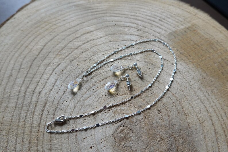 May include: A silver necklace and earrings set with clear crystal teardrop pendants. The necklace is a delicate chain with small silver beads.