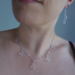 K&ouml;nnte beinhalten: Eine silberne Halskette mit einer zarten Kette und mehreren tropfenf&ouml;rmigen Kristallen, die daran h&auml;ngen. Die Halskette wird von einer Person mit einem schwarzen Tanktop getragen.