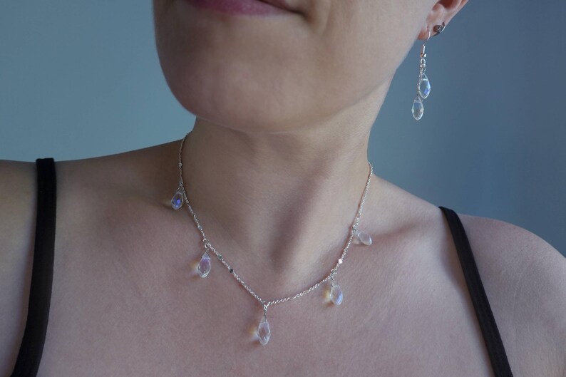 K&ouml;nnte beinhalten: Eine silberne Halskette mit einer zarten Kette und mehreren tropfenf&ouml;rmigen Kristallen, die daran h&auml;ngen. Die Halskette wird von einer Person mit einem schwarzen Tanktop getragen.