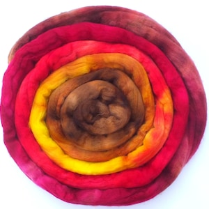 May include: A coiled bundle of wool roving, displaying a vibrant gradient of colours. The centre is a dark brown, shifting through yellow, orange, and red tones, with a magenta outer layer. Ideal for fibre art projects.