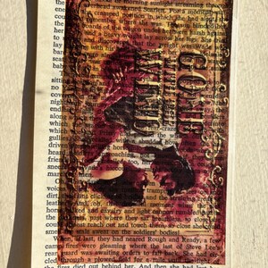 May include: A vintage book with a red, orange, and yellow stained cover. The book is open to a page with text about a journey and a soldier. The text is partially obscured by a red and black image of a soldier.