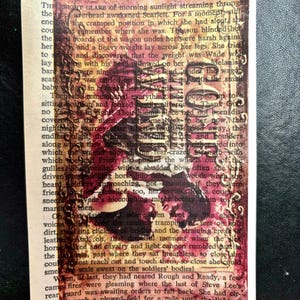 May include: A vintage book page with a red, orange, and yellow paint splatter effect. The text on the page is from a novel titled "Gone With The Wind" by Margaret Mitchell. The text reads "CHAPTER XXIV" and "The bright glare of morning sunlight streaming through the overhead awakened Scarlett. For a moment, still in the cramped position in which she had slept, she could not remember where she was. The sun blinded her and a heavy weight lay across her legs. She tried to move and discovered that the weight was Wade who was sleeping with his head plowed on her knees. Melanie was almost in hot face and under the wagon seat, Prissy was curled up like a block of ice with the small baby wedged in between her and Wade."