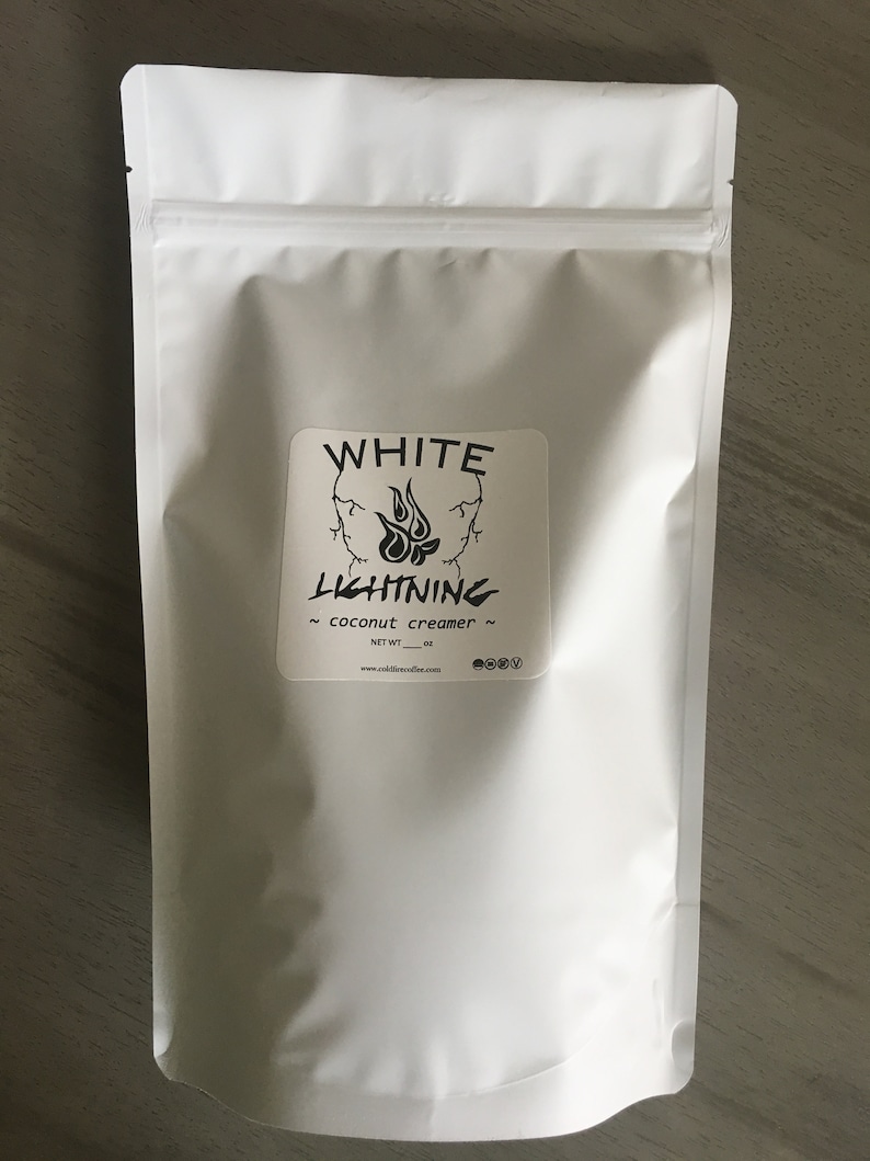 May include: A white, resealable pouch of coconut creamer. The label features the text "WHITE LIGHTNING" above a flame graphic. The words "coconut creamer" are below the graphic. The net weight is listed in ounces. The website address is also printed on the label.