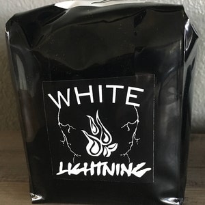 May include: A black package with a white label featuring the words "WHITE LIGHTNING" in a bold font. The label also includes a stylized flame design and lightning bolt graphics.