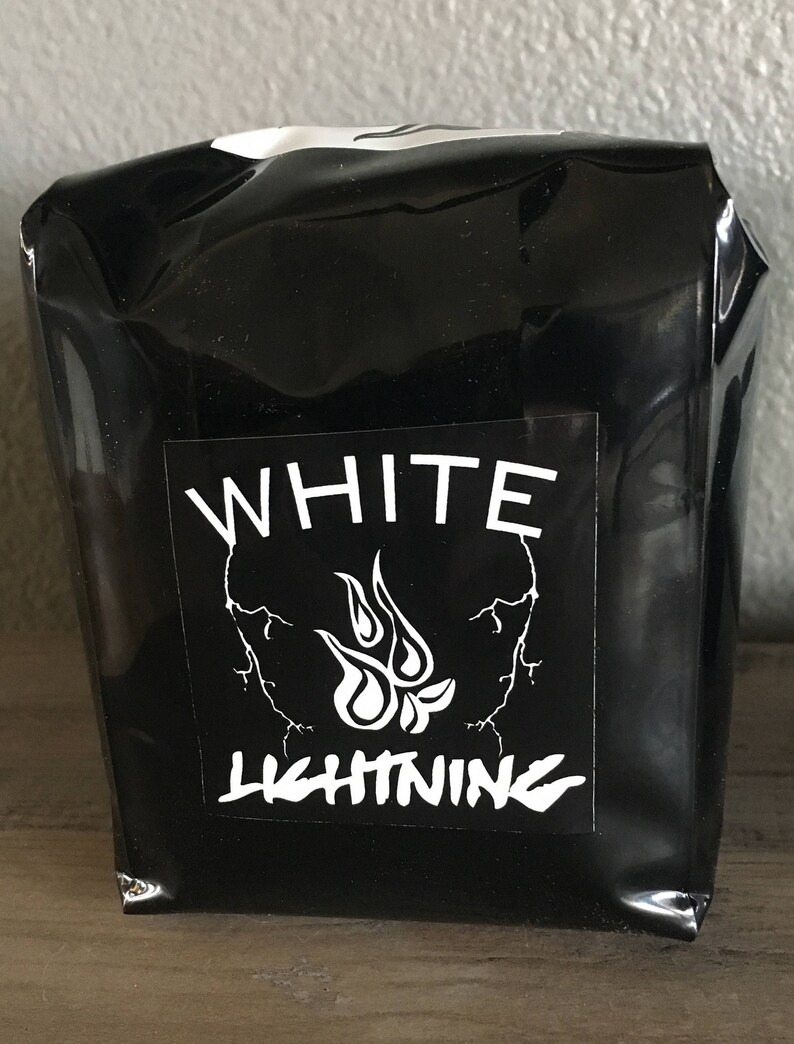 May include: A black package with a white label featuring the words "WHITE LIGHTNING" in a bold font. The label also includes a stylized flame design and lightning bolt graphics.