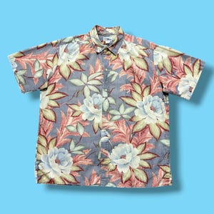 May include: Short-sleeved button-down shirt with a floral pattern. The shirt features large white and light blue flowers, red and green leaves, and a light blue background. The shirt is made of a lightweight fabric.