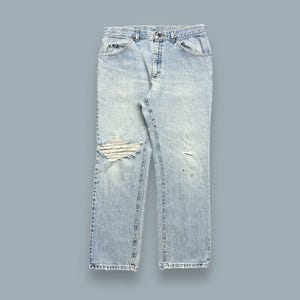May include: Light blue denim jeans with distressed details, including a large hole on the left knee and smaller holes on the right leg.