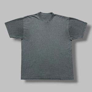 Pode incluir: Uma t-shirt de manga curta em cinzento-carvão escuro sólido com decote redondo. A peça apresenta um design simples e sem padrões, com costuras visíveis ao longo das mangas, da bainha e da gola, oferecendo um corte padrão e uma textura de tecido uniforme.