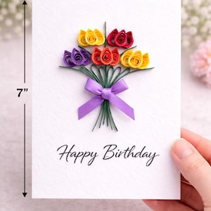 May include: A handmade birthday card, 12.7 cm wide and 17.8 cm tall, features a bouquet of colorful paper flowers in yellow, red, orange, and purple. The bouquet is tied with a purple ribbon. The words "Happy Birthday" are written below.