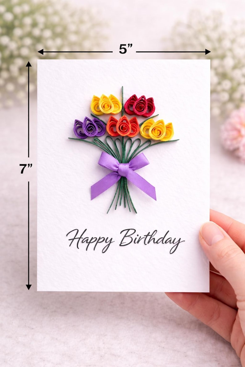 May include: A handmade birthday card, 12.7 cm wide and 17.8 cm tall, features a bouquet of colorful paper flowers in yellow, red, orange, and purple. The bouquet is tied with a purple ribbon. The words "Happy Birthday" are written below.