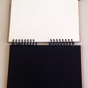 May include: A black and white spiral bound notebook with a cardboard cover. The notebook is open to reveal a blank white page on the left and a black page on the right.