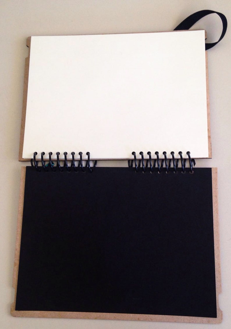 May include: A black and white spiral bound notebook with a cardboard cover. The notebook is open to reveal a blank white page on the left and a black page on the right.