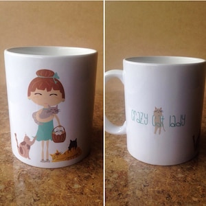 K&ouml;nnte beinhalten: Wei&szlig;e Keramiktasse mit einer Cartoon-Illustration einer Frau mit roten Haaren, die eine Katze h&auml;lt. Die Tasse hat auch eine Cartoon-Katze an der Seite und den Text "Crazy Cat Lady".