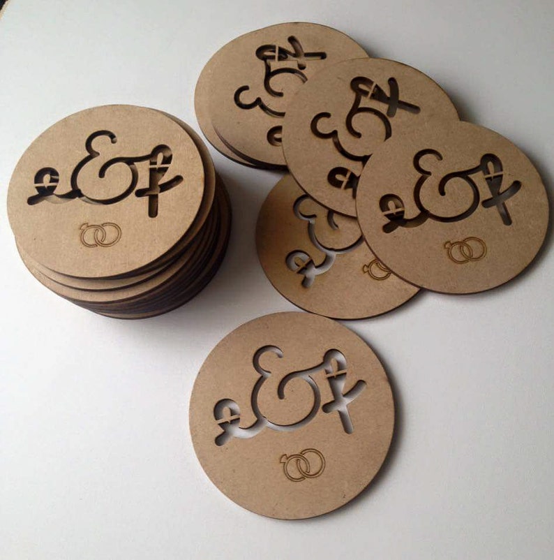 May include: A stack of round, brown wooden coasters with the letters "E & F" and two interlocking rings engraved on them.