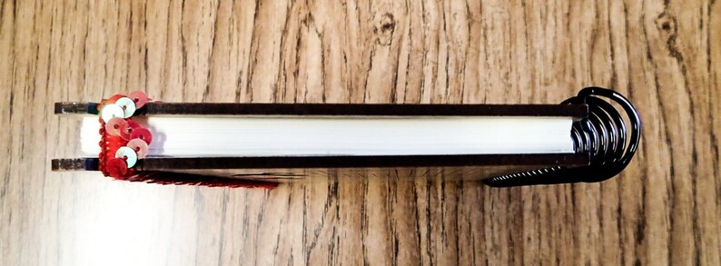 May include: A black spiral bound notebook with a red and white sequin embellishment on the front cover.