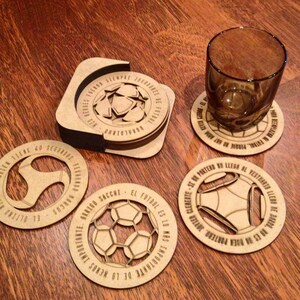 May include: Set of six wooden coasters with a soccer theme. Each coaster features a different design with a soccer ball and Spanish text. The text on the coasters reads: "Mis Herres", "Arrego Sacchi", "El Futbol Es Lo Mas Importante De Lo Menos", "Javier Clemente Se Be Portero No Llega Al Vestuario Lleno De Buena Portero", "El Ultimo Tiene 60 Segundos", and "Narcos".