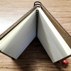 May include: A brown wooden notebook with a spiral binding and blank white pages. The notebook is open and lying flat on a wooden surface.