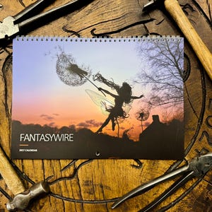 May include: A 2027 wall calendar titled FANTASYWIRE featuring a silhouette of a winged figure holding a dandelion against a sunset sky. The calendar is spiral-bound at the top and displays the text FANTASYWIRE and 2027 CALENDAR on the front cover.