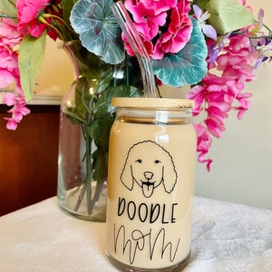 May include: A glass can with a bamboo lid and a glass straw. The can has a black and white doodle of a dog with the text "Doodle Mom" on it.