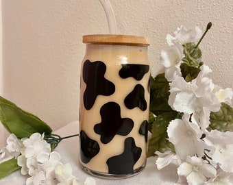 May include: A glass drinking jar with a black and white cow print design. The jar has a bamboo lid and a clear glass straw.
