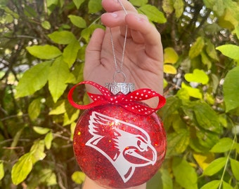 May include: Red and white Christmas ornament with a white cardinal silhouette. The ornament is covered in red glitter and has a red ribbon with white polka dots.