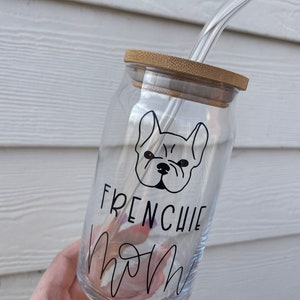 May include: A clear glass water bottle with a bamboo lid and a black and white illustration of a French bulldog with the text "Frenchie Mom" on the side. The bottle has a glass straw.