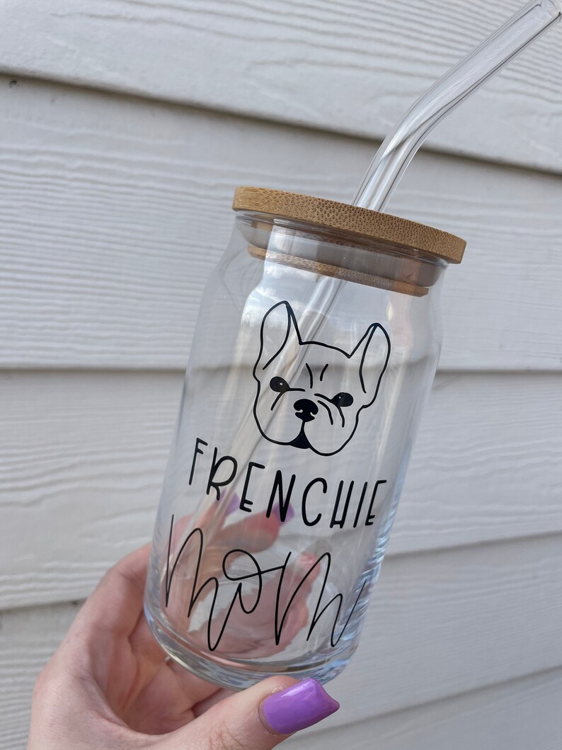 May include: A clear glass water bottle with a bamboo lid and a black and white illustration of a French bulldog with the text "Frenchie Mom" on the side. The bottle has a glass straw.