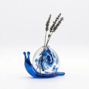 Peut inclure: Un vase en forme d'escargot en verre, avec un corps transparent et des accents bleus. Le corps de l'escargot est un globe de verre transparent avec des tourbillons et des taches bleues. La tête et la queue de l'escargot sont bleu vif. Le vase contient des tiges de lavande séchées.