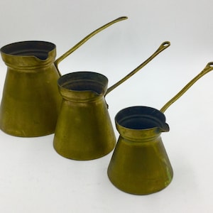 May include: Three brass coffee pots of varying sizes with long handles. The pots are all shiny and have a traditional design.