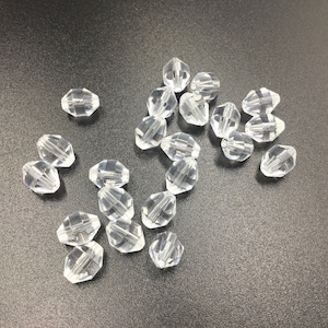 May include: A group of clear glass beads with a faceted design. The beads are scattered on a dark gray surface.