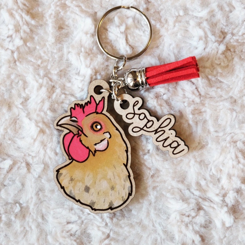 May include: A wooden keychain with a red tassel, a chicken charm, and a wooden tag with the name "Sophia" written on it.