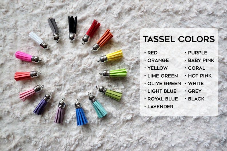 May include: A variety of colors of tassel keychains, including red, orange, yellow, lime green, olive green, light blue, royal blue, lavender, purple, baby pink, coral, hot pink, white, grey, and black. The tassels are arranged in a circle on a white fuzzy surface. The text "TASSEL COLORS" is written in black at the top of the image.