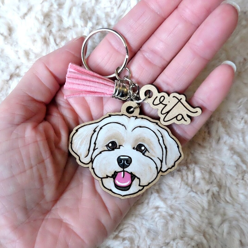 May include: A white dog keychain with a pink tassel and the name "Rita" written on a wooden tag.